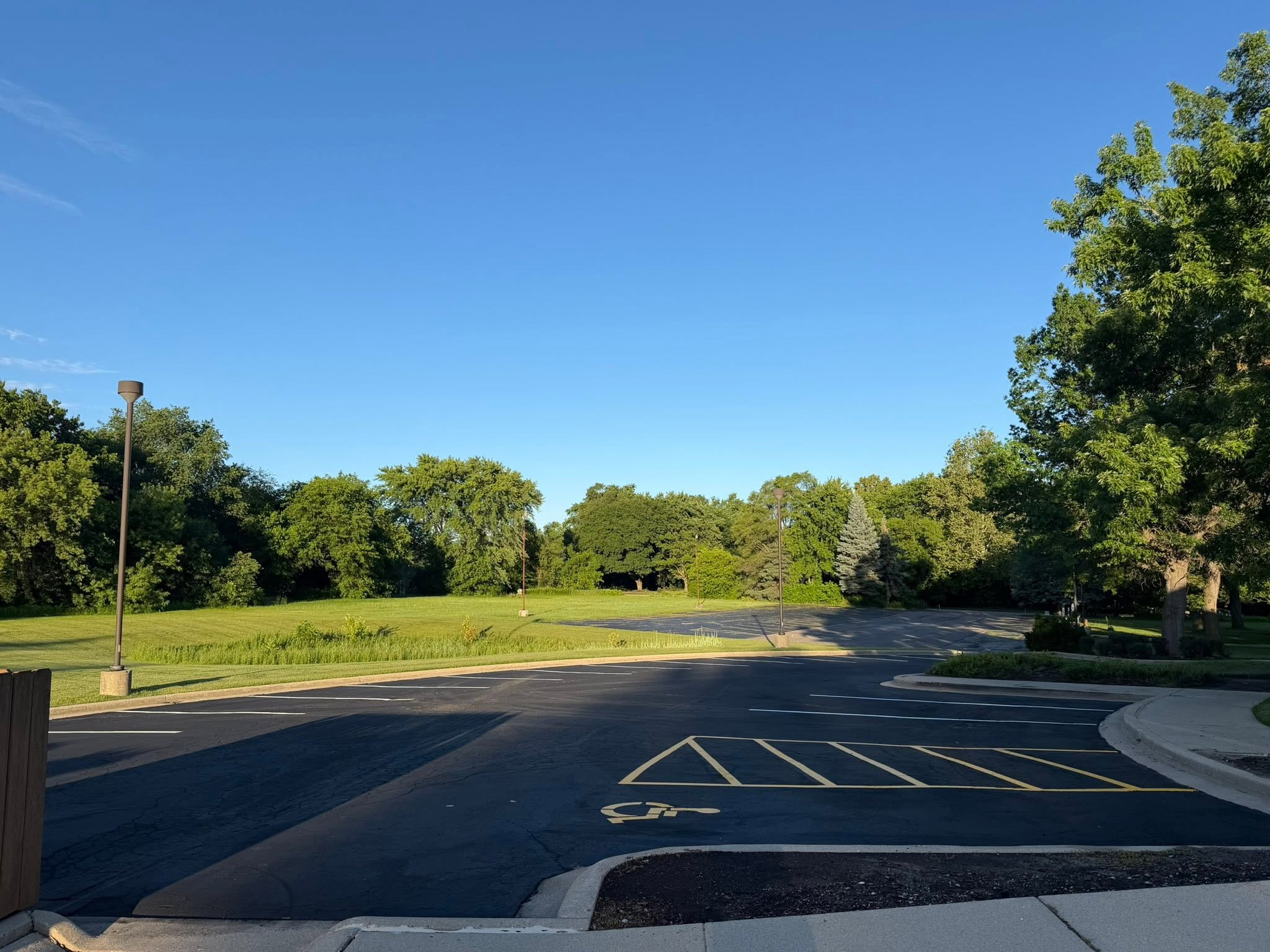 Freshly sealed and striped parking lot beside a tree-lined lawn